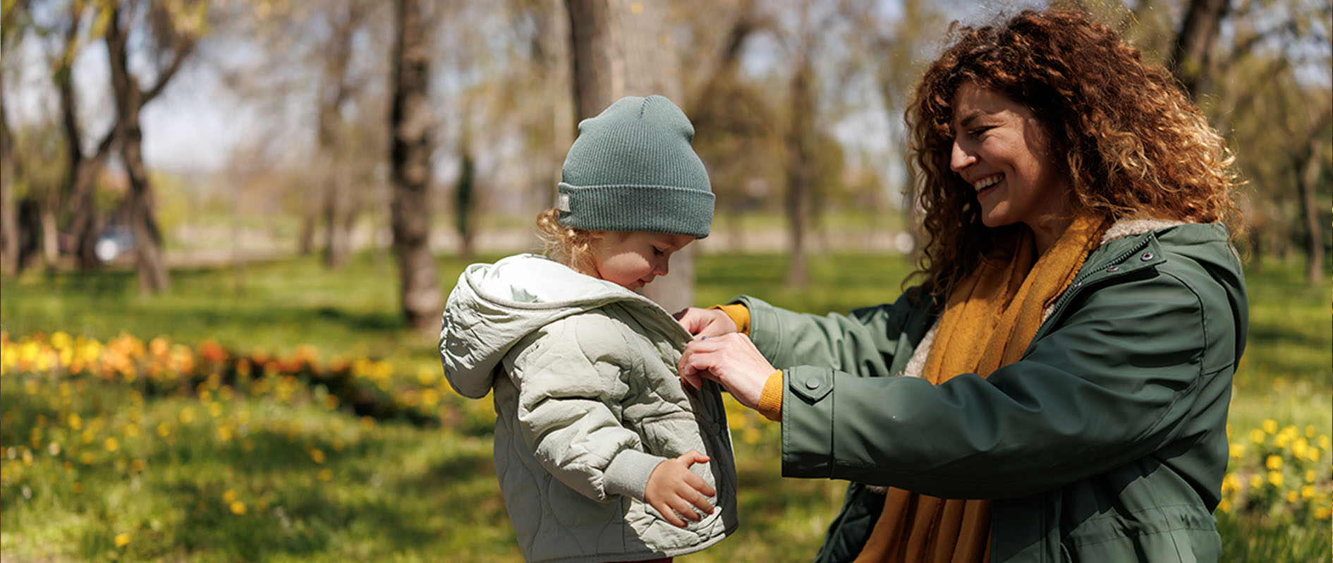 Caring mother buttoning her daughter's jacket during cold early spring day in the park 